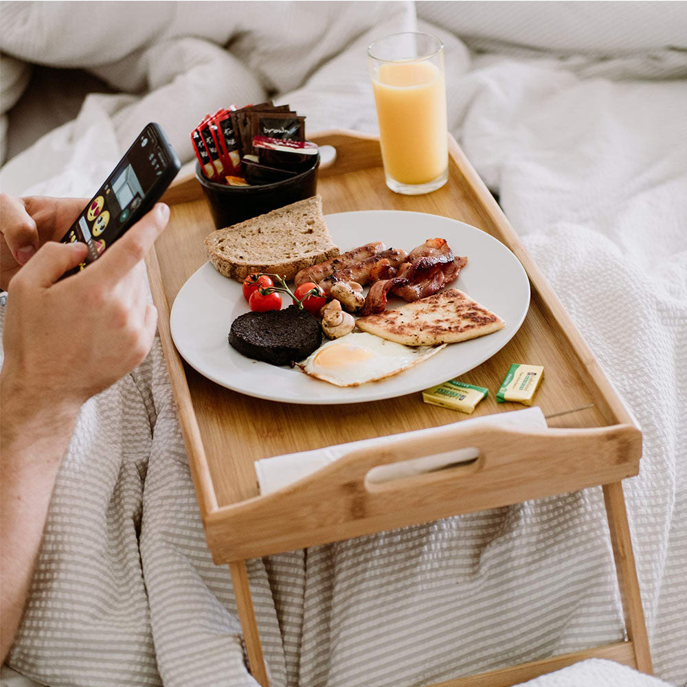 Bags Direct Eco-Friendly Bamboo Bed Serving Tray with Stand - 784200240 - showcasing its use by serving someone in bed. The fold out legs provide support and stability when you're lying in bed and eating